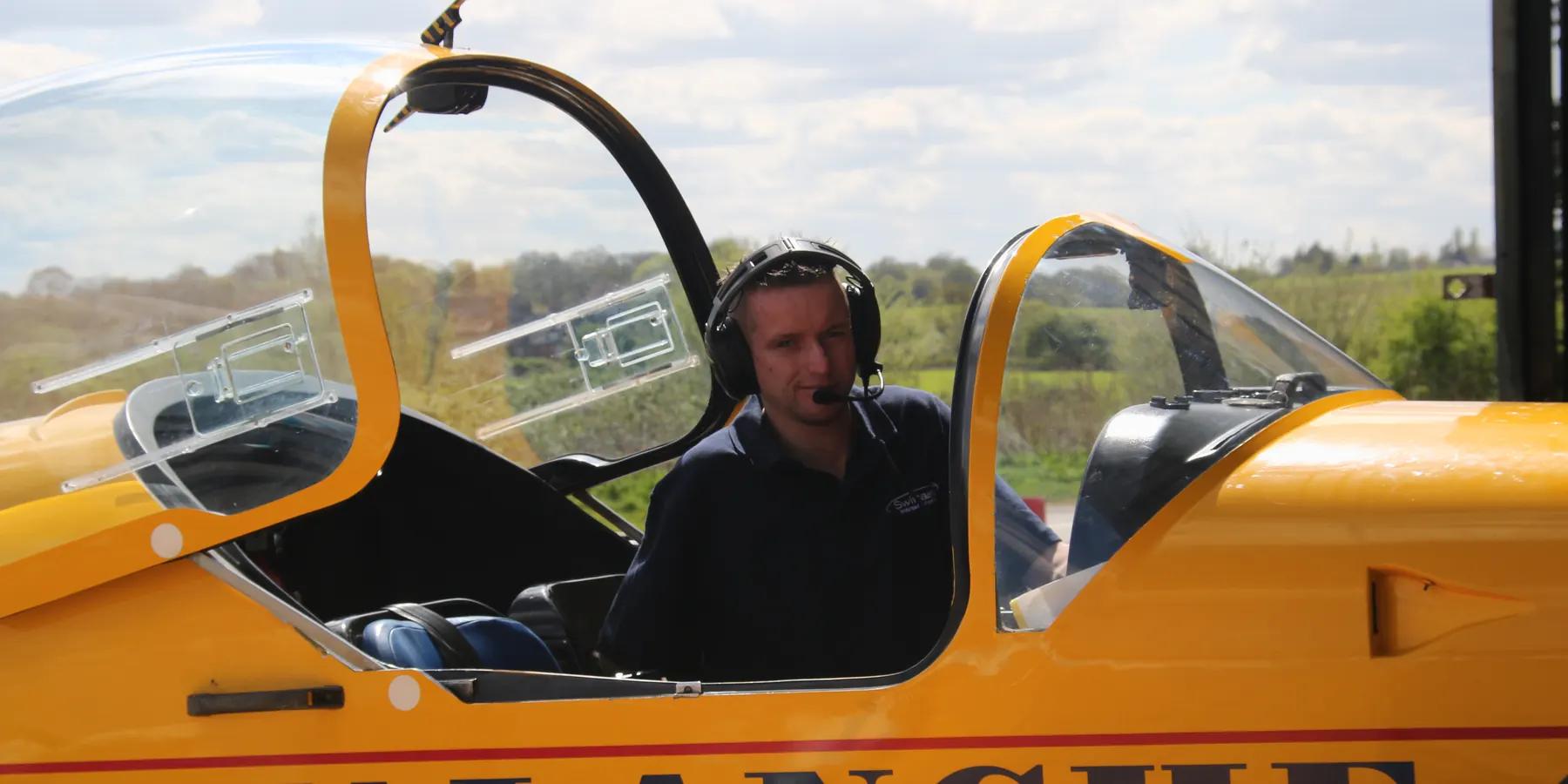 Pilot in the open cockpit of a yellow Slingsby aircraft on the apron