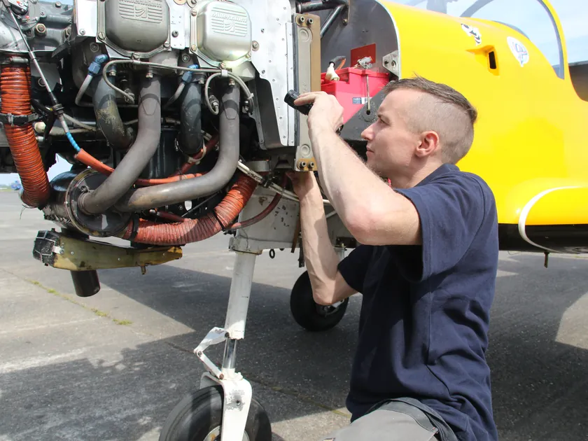 Engineer working on the exposed engine of a yellow Slingsby aircraft